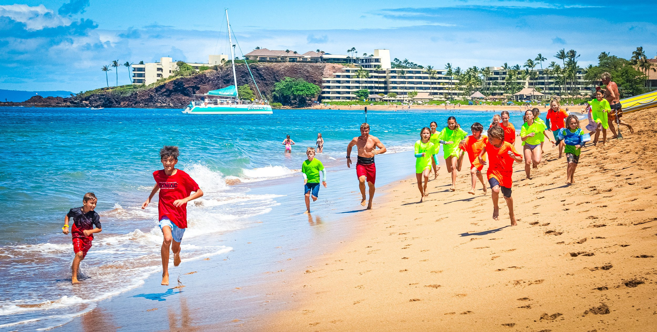Kahakukahi children and adults run together along a Maui beach.