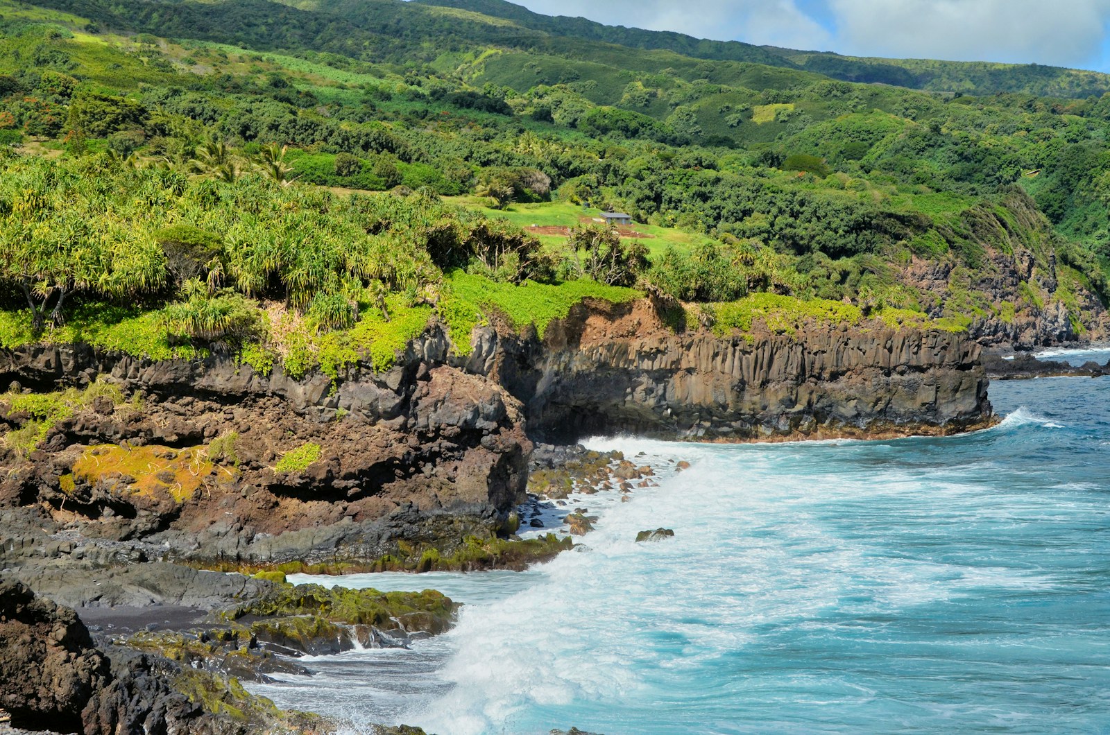 Lush green coastline and turquoise surf in Hāna, Maui, photographed by Jeffrey Eisen.